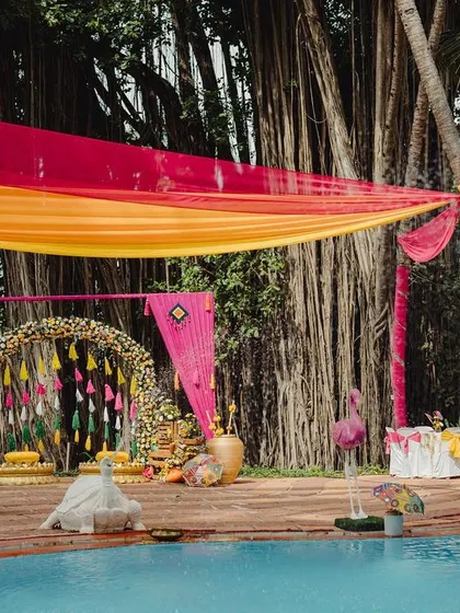 A vibrant poolside Haldi setup, with colorful drapes and a beautiful floral arch, creating a festive atmosphere for this destination wedding.