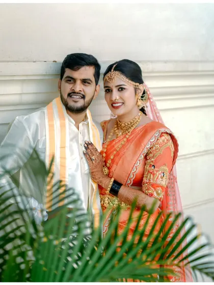 A classic wedding portrait of a couple, framed by green leaves, their happy smiles directed at the camera.