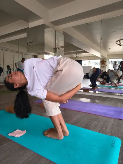 This student demonstrates a deep forward fold with a bind, a pose that requires both flexibility and strength. Our TTC curriculum is designed to help students progress safely into such advanced postures.
