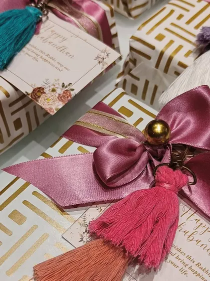 Beautifully wrapped Rakhi gifts with a personal touch. Each present is adorned with a colorful tassel keychain and a 'Happy Rakshabandhan' card.