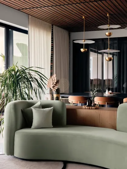 A curved sage green chaise lounge provides a beautiful, sculptural seating element. The view looks towards the dining area and balcony, showcasing the open and light-filled layout of the home.
