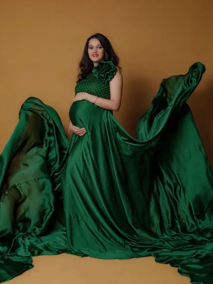 This stunning emerald green satin maternity gown has a dramatic, flowing trail. It’s a one-shoulder design with a floral detail, perfect for creating artistic shots.