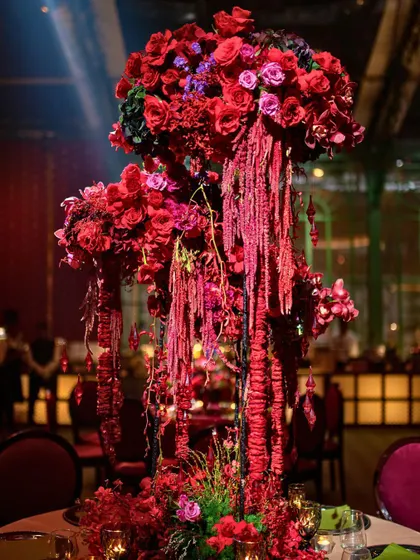 A dramatic centerpiece for a dining table, featuring a towering arrangement of red flowers with cascading amaranthus.