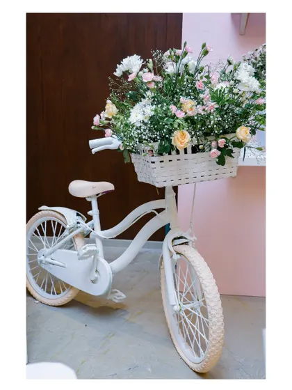 A classic white bicycle with a basket of fresh flowers serves as a beautiful and rustic prop, perfect for a garden, floral, or shabby-chic themed party.