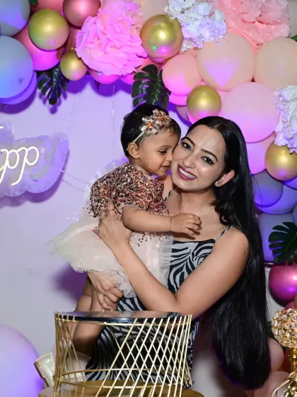 A mother holds her daughter close during her birthday celebration. The soft lighting and beautiful balloon backdrop make this tender moment even more special.