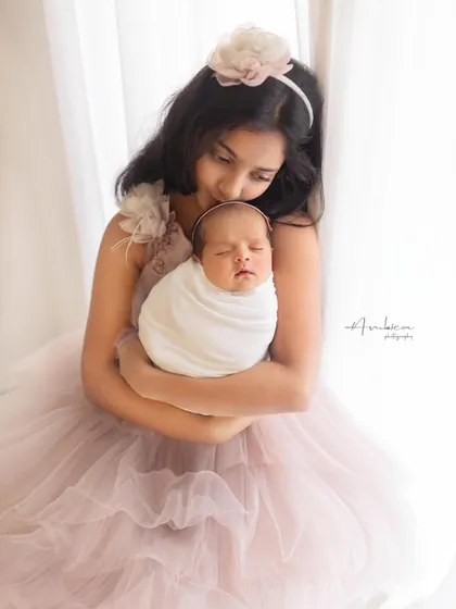 "Mere do anmol Ratan." An older sister holds her newborn sibling, both dressed in soft pink gowns. This is a classic, beautiful portrait capturing the start of a lifelong friendship.