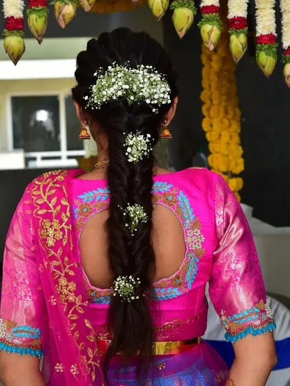 A view of the back of this lovely pink blouse. It features a keyhole cutout and elegant embroidery that matches the work on the sleeves, paired with a beautifully braided hairstyle.