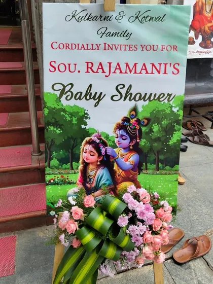 This welcome sign for a baby shower features a beautiful illustration of Radha and Krishna. The fresh flower arrangement at the base adds a touch of elegance and tradition.