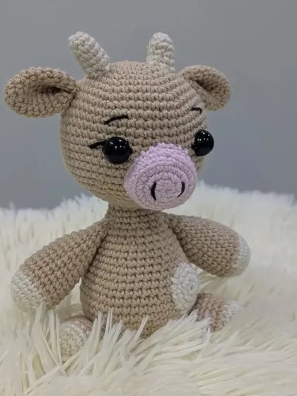 A gentle crochet cow in beige and white, with a soft pink nose.