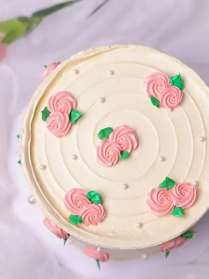 We believe in the timeless beauty of simplicity with this elegant floral cake. A pristine white buttercream canvas is adorned with delicate, hand-piped pink rosebuds and tiny pearls, creating a classic and graceful design perfect for Mother's Day or an anniversary.