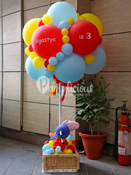 A cheerful balloon arrangement in primary colors with a Peppa Pig toy basket, perfect for a welcome display or gift corner.