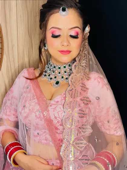 A modern bridal look with a soft pink lehenga and bright pink eyeshadow, paired with a diamond and emerald necklace.