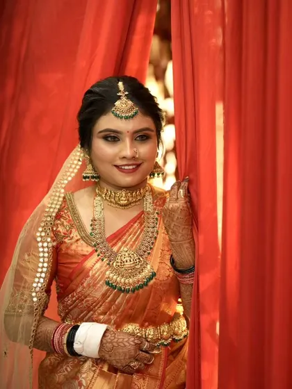 A beautiful portrait of the bride in her orange Kanjeevaram saree. The makeup features a smokey eye and a neutral lip, balancing the vibrant colors of her attire.