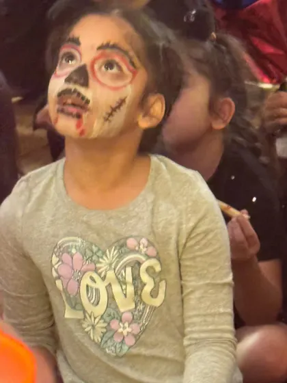 This spooky-cute skeleton face paint is a perfect example of the amazing work our artists do. Look at her expression, completely captivated by the show.