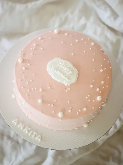 A simple, pretty, and elegant birthday cake that never fails to impress. The soft pink frosting, scattered pearls, and delicate plaque create a timeless and sophisticated look.