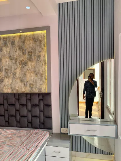 A close-up of a bedroom design showing a textured headboard, a feature wall panel, and a modern dressing unit with a semi-circular mirror against a fluted panel.