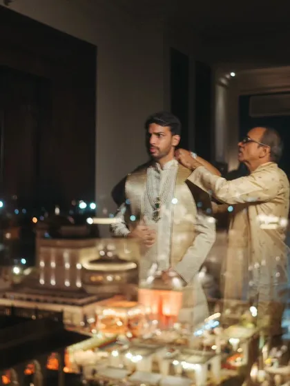 A creative shot of the groom getting ready with his father, with the city lights reflected in the window.
