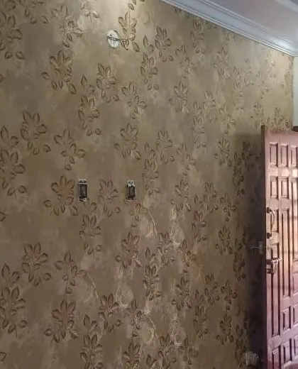 A wall with a dark, textured wallpaper featuring a subtle leaf pattern. The design is elegant and adds a sense of depth.