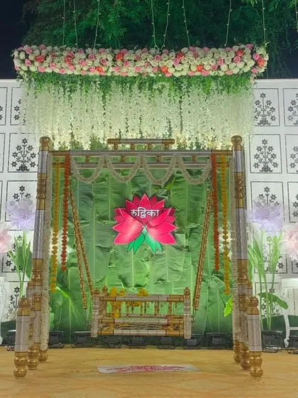 This is a complete stage setup for a traditional naming ceremony. The design centers around the beautifully decorated palna, framed by a fresh green backdrop, hanging florals, and soft lighting to create a peaceful and celebratory atmosphere.