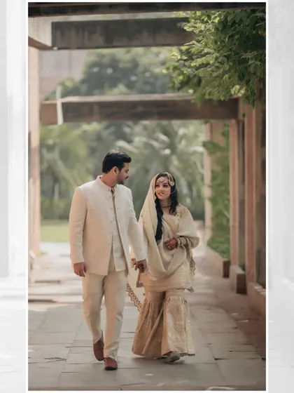 The couple walks hand-in-hand through a sunlit corridor, their smiles and gentle hold capturing a moment of pure, serene love.
