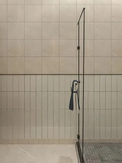 A minimalist shower area with a simple glass partition. The clean lines and neutral tiles create a sense of calm and openness, making the bathroom feel spacious and uncluttered.