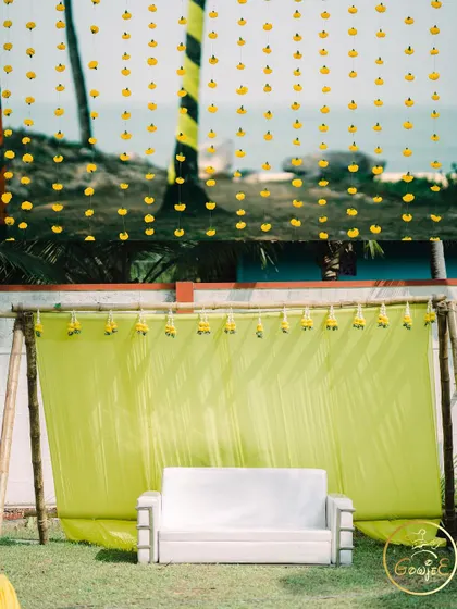 A simple yet elegant Haldi backdrop with a lime green drape and hanging marigold strings.