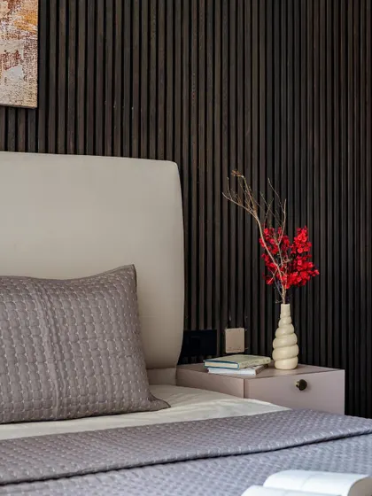 A close-up of the bedside, where a vibrant red floral arrangement provides a pop of color against the dark, reeded wall and neutral bedding.