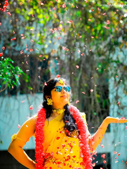 A stylish and fun bridal shot during the Haldi festivities. The sunglasses and flower petals add a playful touch, reflecting the bride's personality and the celebratory mood.
