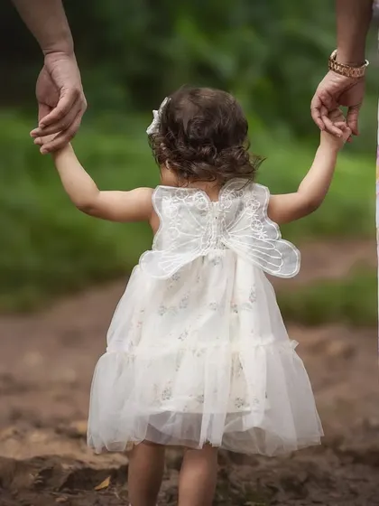 A close-up shot of a toddler holding her parents' hands, taken from behind to emphasize the feeling of being guided and protected. The detail of their linked hands tells a story of family unity.