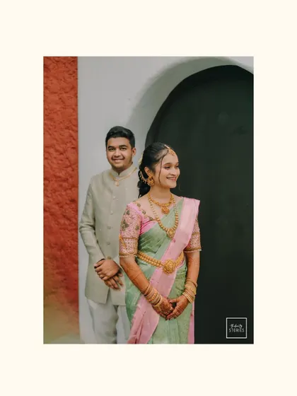 A classic, poised portrait of the couple against a simple, elegant backdrop. The bride's soft green and pink saree complements the groom's cream-colored attire perfectly.