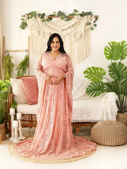 A full-length portrait of a mom-to-be in a lovely pink lace gown. Our boho studio setup with macrame and plants provides a warm and natural setting.