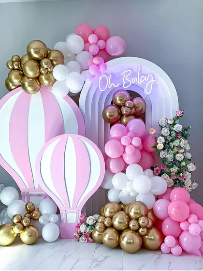 A pink and gold hot air balloon theme, perfect for a baby shower. The combination of pink, white, and metallic gold balloons with the "Oh Baby" neon sign creates a chic and celebratory feel.