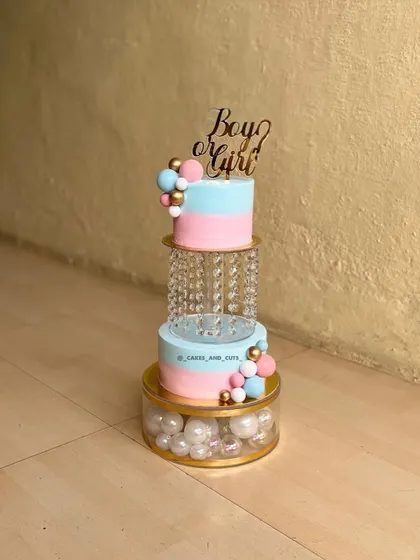 A beautiful two-tier gender reveal cake in pink and blue. This design features a crystal separator filled with pearls and a "Boy or Girl" topper.