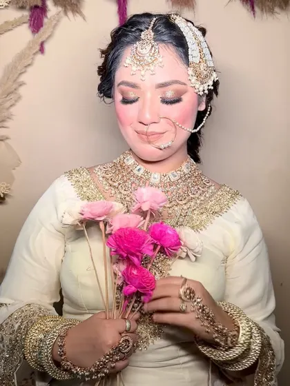 A beautiful bride holding flowers, showcasing a soft and romantic makeup look. The focus is on rosy cheeks and gentle eye makeup.