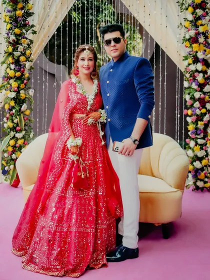 A stylish portrait of the couple at their Mehendi ceremony. The bride's shimmering red lehenga and the groom's royal blue jacket create a striking color combination.