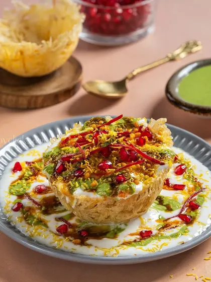 A creative take on Raj Kachori, with a crispy shell filled with yogurt, chutneys, and pomegranate seeds, styled for a modern Indian restaurant.