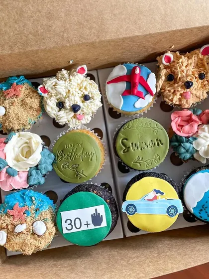 A full box of custom cupcakes with various themes, including travel, pets, and floral designs.