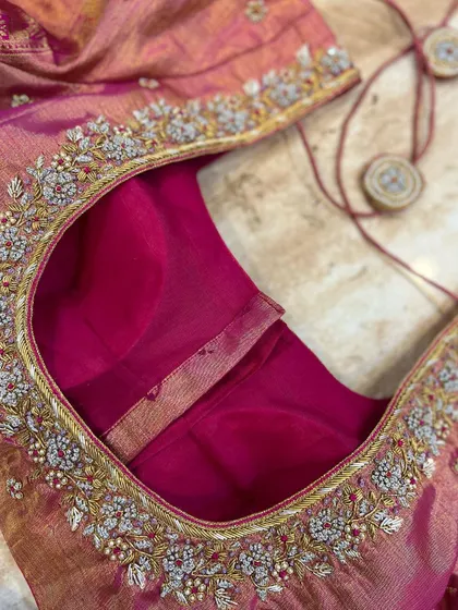 This pink tissue silk blouse features intricate silver and gold floral embroidery along the neckline, giving it a rich and delicate look.