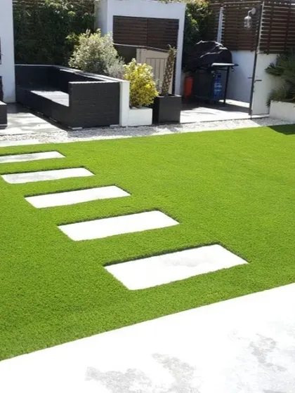 A closer look at a modern patio where artificial turf surrounds large, minimalist stone slabs. This design is both visually striking and highly functional for outdoor living.