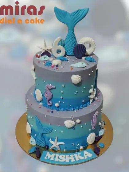 Dive into a magical underwater world with this two-tier mermaid cake. Decorated with shades of blue and purple, it features mermaid tails, seahorses, and seashells for a 6th birthday splash.