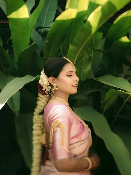 A serene profile shot of a South Indian bride against a backdrop of lush green leaves.