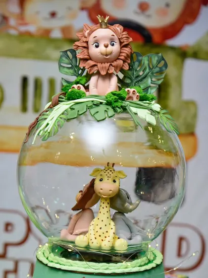 A stunningly detailed jungle-themed cake topper, featuring a lion king sitting atop a glass globe with other safari animals inside.