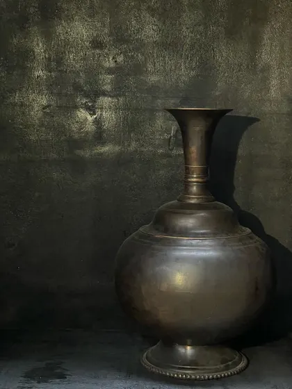 A single large copper vase, its vintage finish highlighted by dramatic lighting. This piece has an exquisite shape and stands as a strong decorative element on its own, perfect for a minimalist setting.