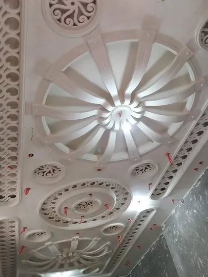 A highly detailed, multi-layered ceiling before painting. You can see the intricate circular patterns, jaali work, and radial designs that give it a palatial feel.