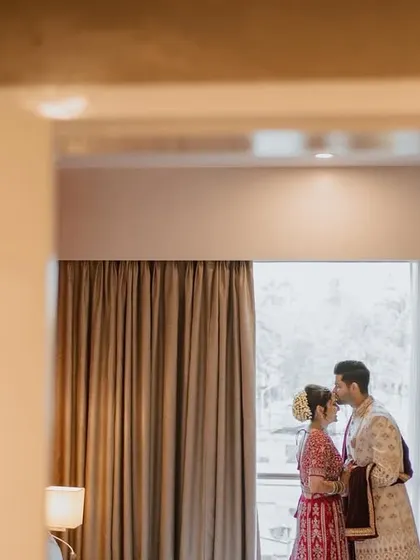 A tender moment as the groom kisses his bride's forehead, framed beautifully within a doorway for a private, cinematic feel.