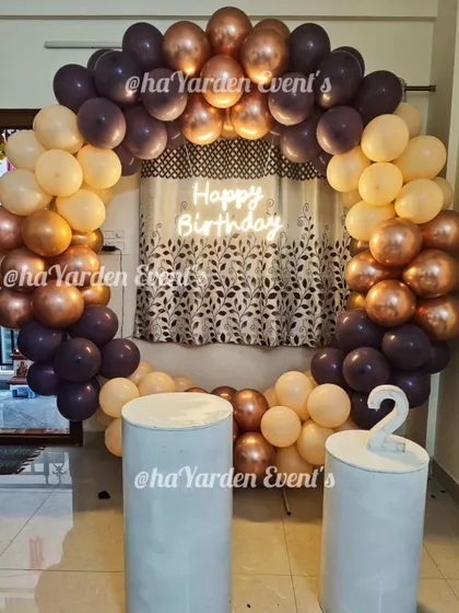 A simple and sophisticated balloon ring in muted, earthy tones. The 'Happy Birthday' neon sign adds a modern touch to this cozy home setup.