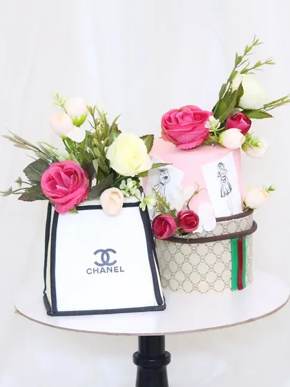 A fashion lover's dream, this cake is designed to look like luxury gift boxes and bags. It features a Chanel-inspired bag and a Gucci-style hat box, both adorned with beautiful fresh flowers.