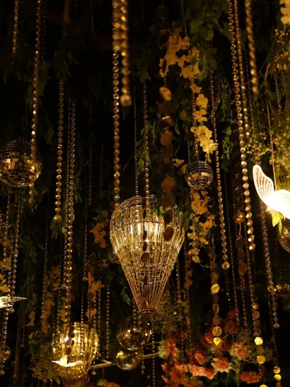 A detailed shot of the sangeet ceiling, showing the mix of greenery, crystal chandeliers, and golden accents.