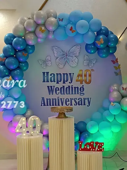 Celebrating a 40th wedding anniversary in style. This beautiful setup includes a circular backdrop, a blue and silver balloon arch with butterfly details, and light-up marquee numbers.