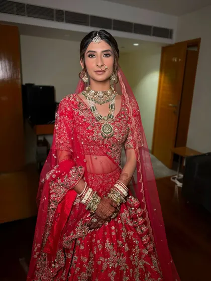 A classic bridal portrait of Yashvi. Her makeup features defined eyes and a soft matte lip, creating a sophisticated and modern bridal look that perfectly matches her red Dolly J Studio lehenga.